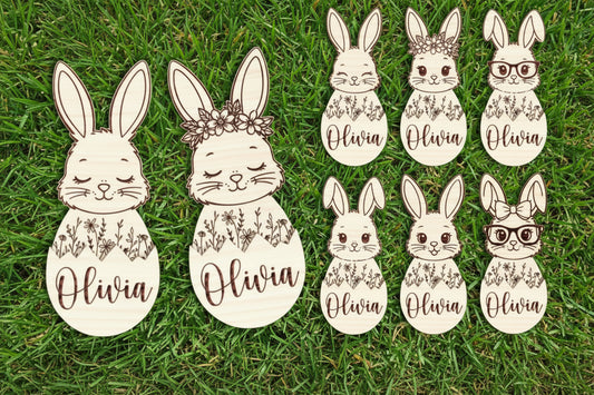 Set of bunny face cutouts with floral designs and the name  on a wooden background.